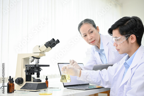 Asian male scientist adjust a chemical liquid in a conical beaker and working with his colleagues