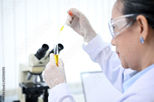 Professional-aged Asian female chemist dropping a chemical liquid into a test tube