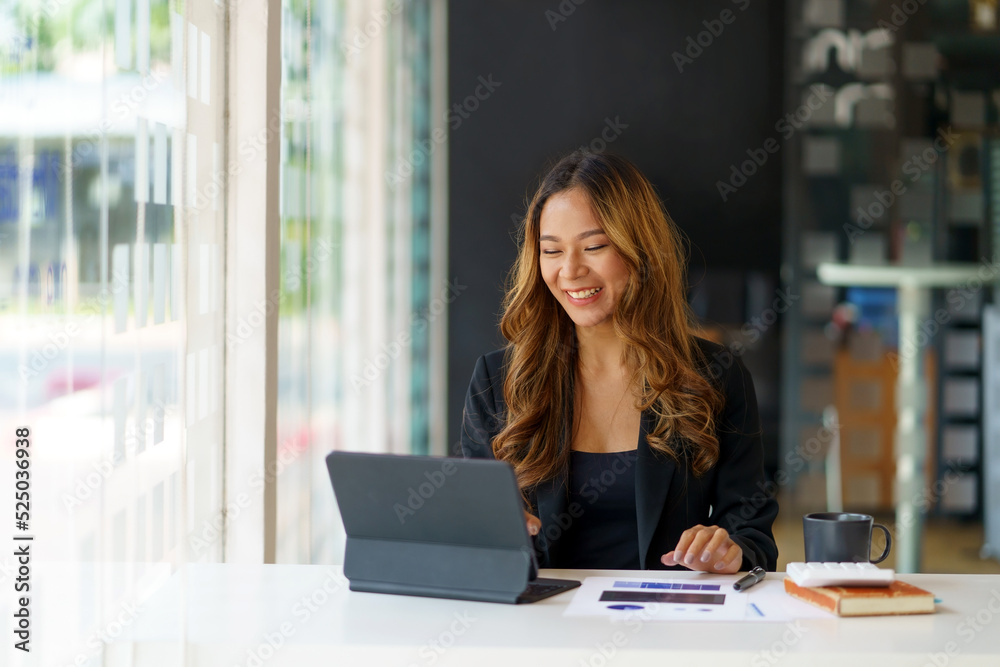 Beautiful Asian businesswoman using her laptop enjoys working, taking notes, reviewing assignments and enjoy reading.