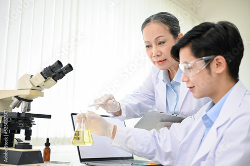 Professional Asian middle-aged female scientist training a young male scientist in the lab.