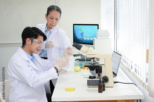 A talented Asian male scientist doing an experiment in the lab while inspected by his supervisor.