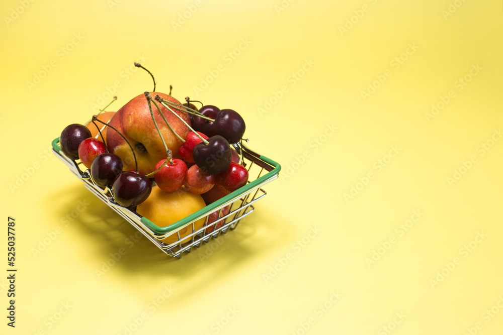 A grocery basket filled with various fruits - bananas, cherries, nectarines, apricots, peaches on a bright yellow background kopi space. A grocery basket filled with various fruits - bananas, cherries, nectarines, apricots, peaches on a bright yellow background kopi space.