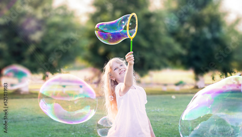 Child girl plays, inflates bubbles in the garden.