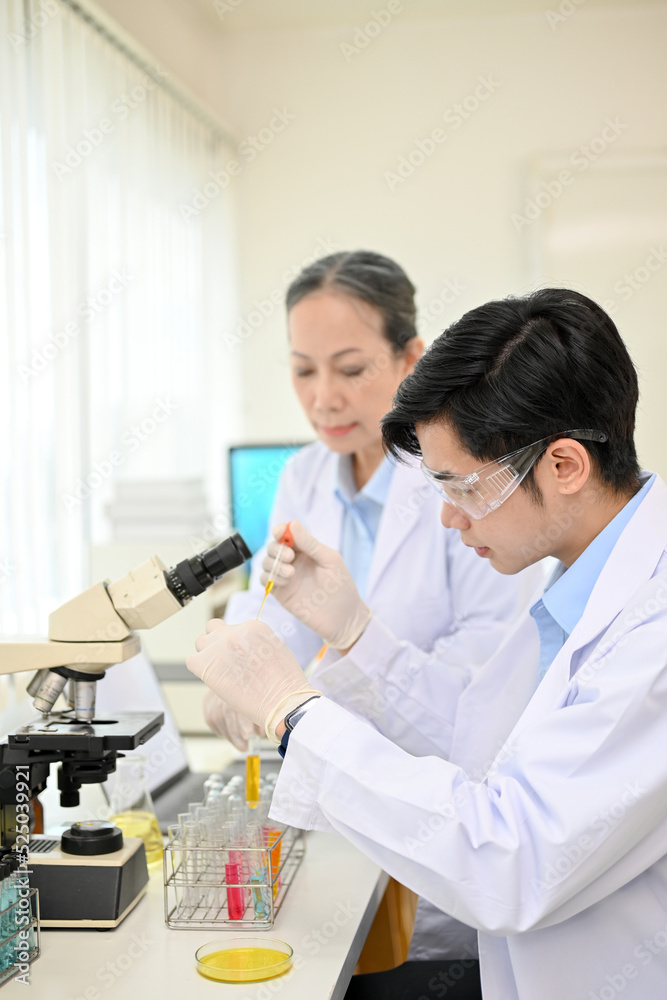 Concentrated Asian male scientist working in the laboratory with his coworker. Concentrated Asian male scientist working in the laboratory with his coworker.