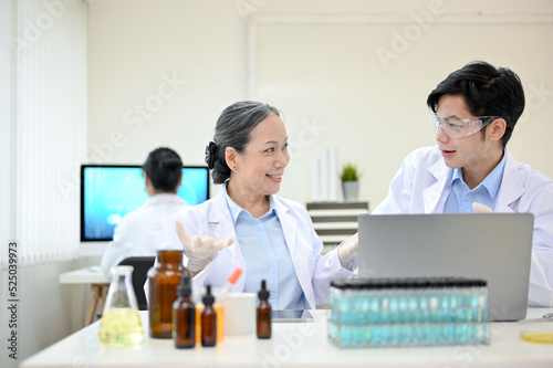 Cheerful Asian middle-aged female scientist working in the lab with her young male coworker.