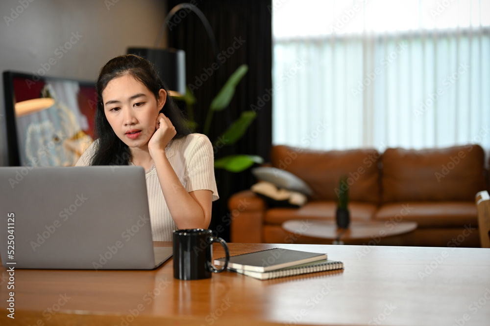 Concentrated young Asian female college student remote working from home, using laptop. Concentrated young Asian female college student remote working from home, using laptop.