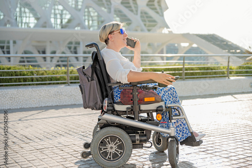 portrait of a smiling woman sitting in an electric wheelchair talking on a mobile phone photo