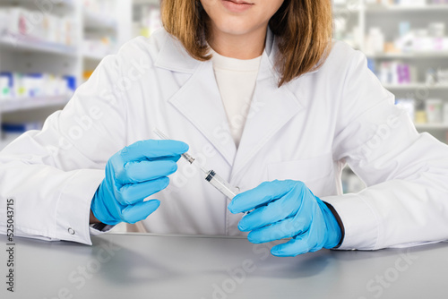 Young woman pharmacist holding syringe with medication whileworking in pharma store