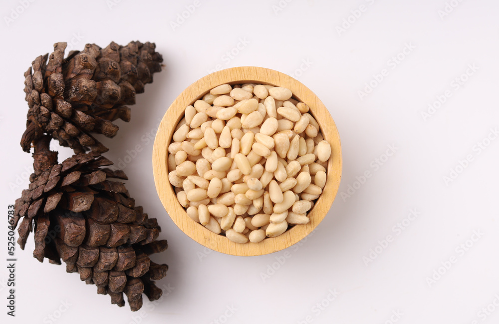 Heap of pine nuts and wood cup and cedar cones on white background Heap of pine nuts and wood cup and cedar cones on white background