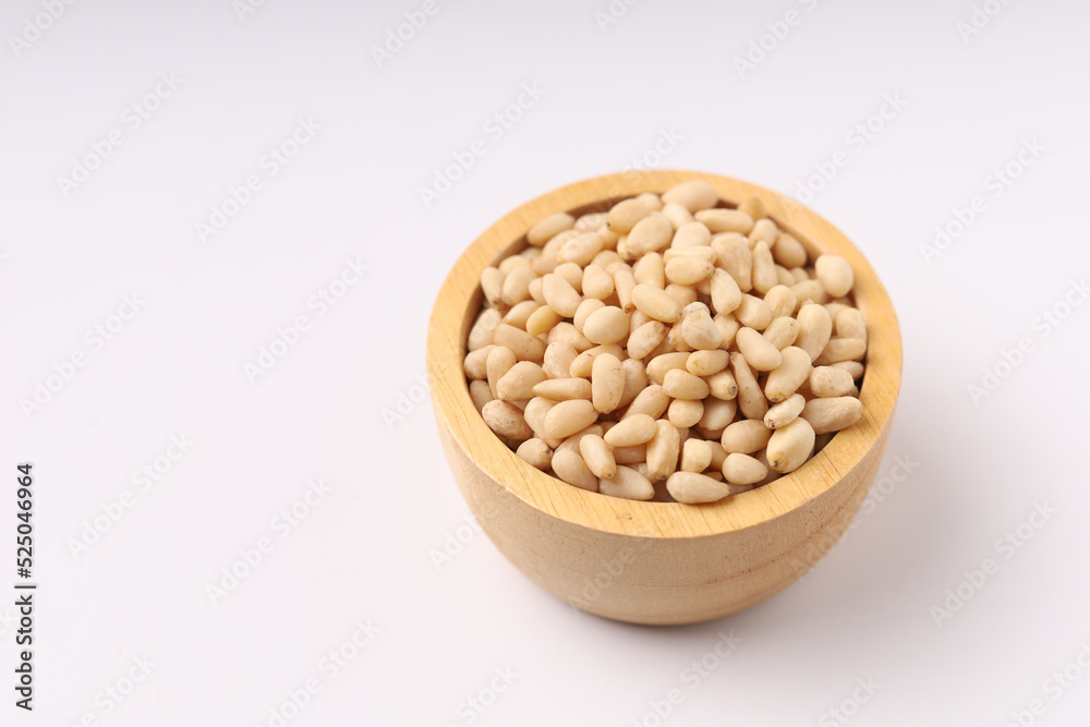 Heap of pine nuts and wood cup and cedar cones on on white background