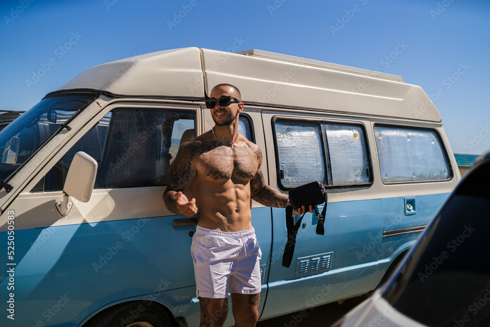 Φωτογραφία Chico tatuado musculoso apoyado en una furgoneta en verano junto a la playa sin