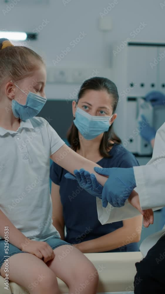 Vertical video: Medic doing palpation consultation on little girl at checkup visit, examining injured arm to give treatment and medicine. Physician consulting small child in office during covid 19 Vertical video: Medic doing palpation consultation on little girl at checkup visit, examining injured arm to give treatment and medicine. Physician consulting small child in office during covid 19