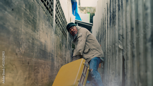 A homeless Asian man is dragging a large suitcase in a narrow alley. to find jobs and food from people who will donate An elderly man with no work, no home, and on the roadside. © Ekkasit A Siam