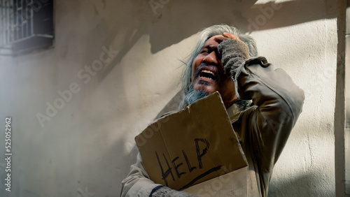 A dirty-dressed Asian old man holding a sign with a message for help, stressed out because he has no work and no food, has to constantly lie on the side of the road. Homeless do not have home