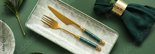 Elegant table setting with golden cutlery on green background