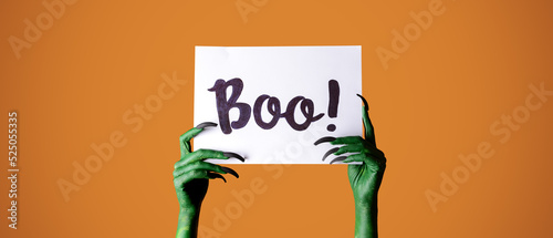 Foto Hands of witch holding paper with text BOO on orange background