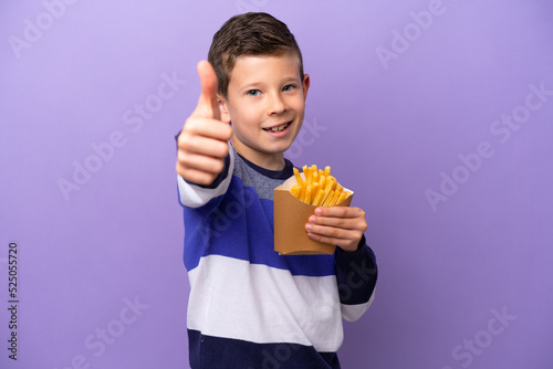 Little boy holding fried chips isolated on purple background with thumbs up because something good has happened