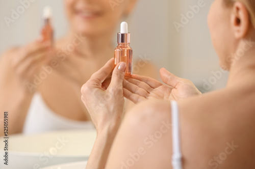 Mature woman using cosmetic serum in bathroom  closeup