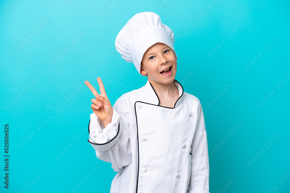 Little chef boy isolated on blue background smiling and showing victory sign Little chef boy isolated on blue background smiling and showing victory sign