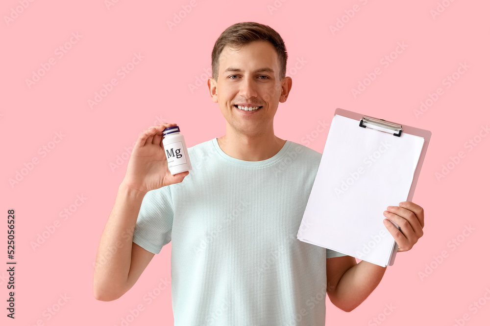 Young man with bottle of magnesium pills and clipboard on pink background - obrazy, fototapety, plakaty 