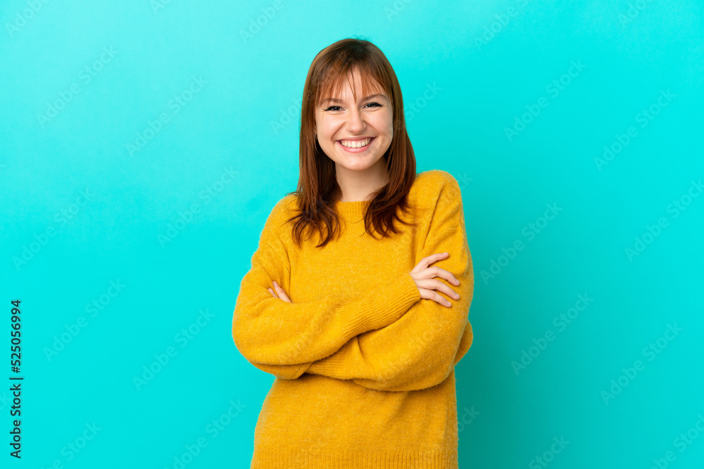 Obraz premium Redhead girl isolated on blue background keeping the arms crossed in frontal position