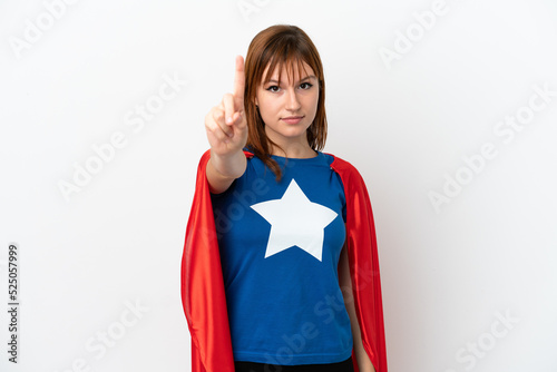 Redhead girl isolated on white background in superhero costume and pointing to the front