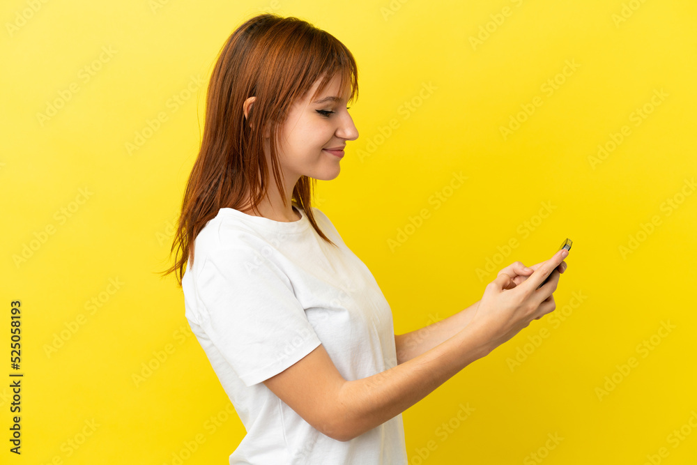 Redhead girl isolated on yellow background sending a message or email with the mobile Redhead girl isolated on yellow background sending a message or email with the mobile