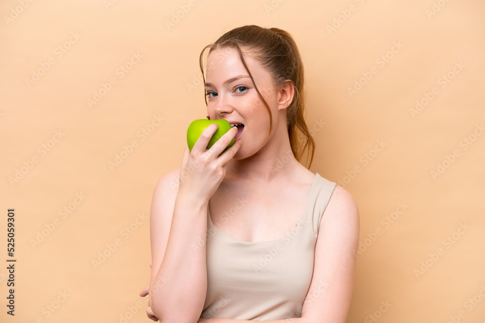 Young caucasian girl isolated on beige background eating an apple Young caucasian girl isolated on beige background eating an apple