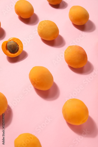 Half of apricot among whole ones on pink background