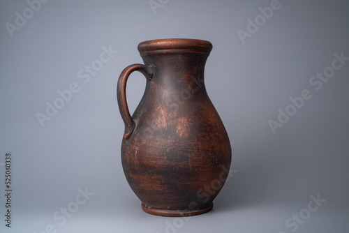 Dark brown jug with a handle, handmade jar from clay on a gray background in the studio. Earthenware for drink and food. Kitchen utensils. Old rustic cookware made of earthen. Retro craft vessel.