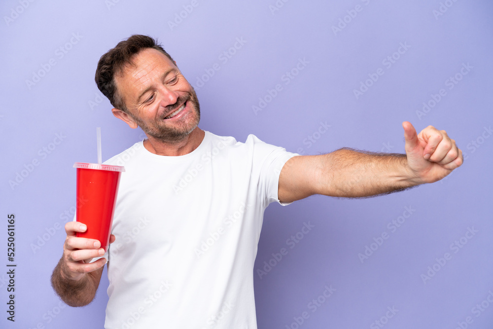 Middle age caucasian man holding soda isolated on purple background giving a thumbs up gesture Middle age caucasian man holding soda isolated on purple background giving a thumbs up gesture