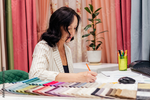 Mature woman designer sketching at fabric store indoor. Woman choosing fabric and furniture for curtain indoor