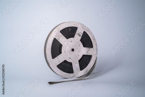 Old scratched metal reel with audio or video tape on a gray studio background. Bobbin, retro magnetic spool. Round reel for analogue projector or sound record. Videotape, filmstrip.