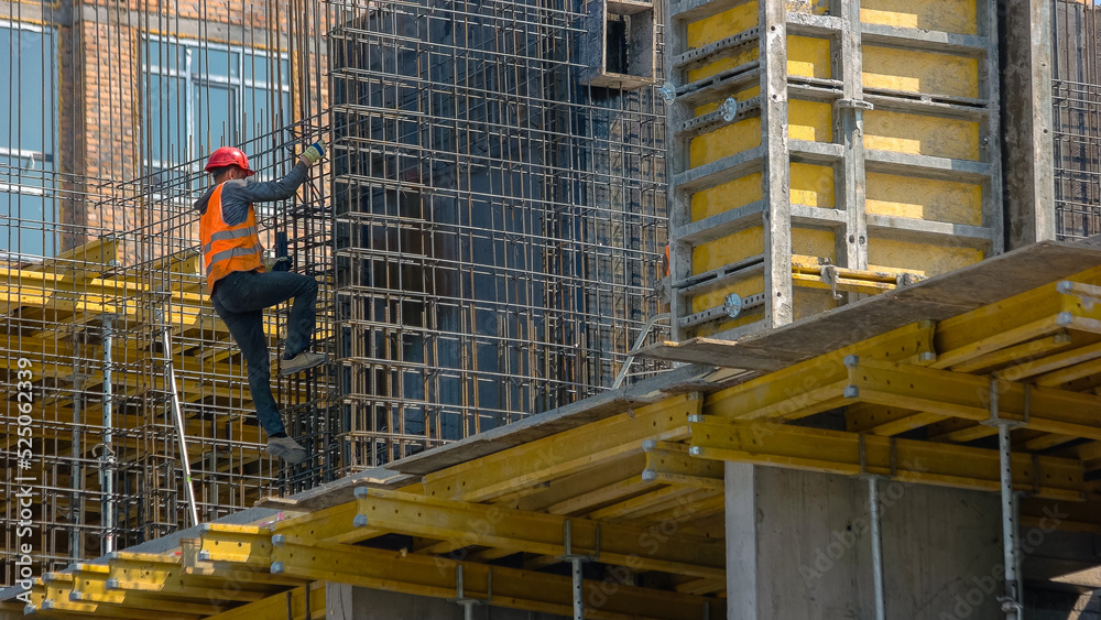Worker on the skyscraper construction site. Employeed man in the orange vest.