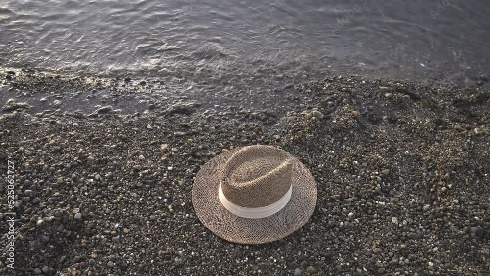 Straw hat on beach water edge with small stones and available copy space Straw hat on beach water edge with small stones and available copy space