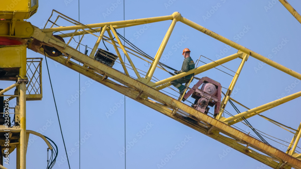 Construction worker builder sits on the yellow crane. Happy engineer feel success after good work.