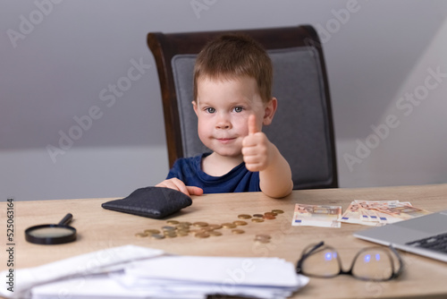 A boy in a blue t-shirt sits at a table with money