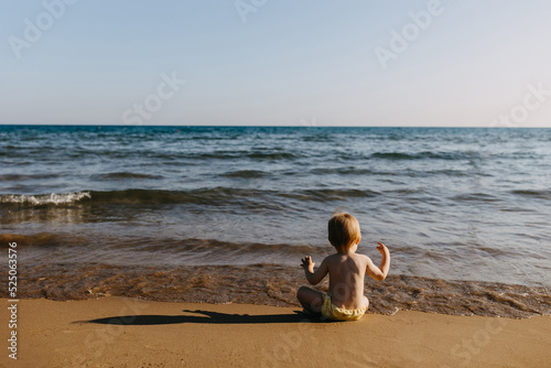 Little child sitting alone on a seashore, watching waves