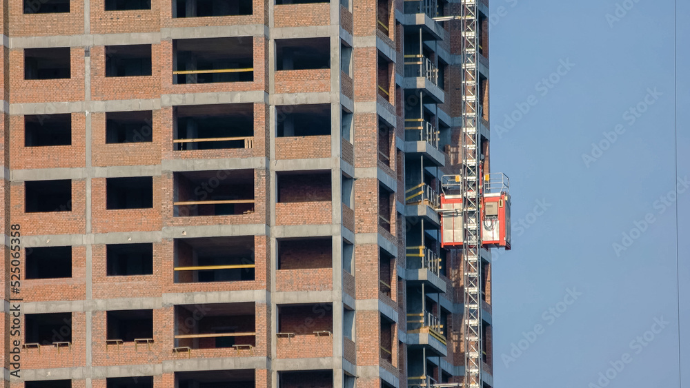 Building under construction with an elevator lift. Workers moving down with an elevator. Building under construction with an elevator lift. Workers moving down with an elevator.