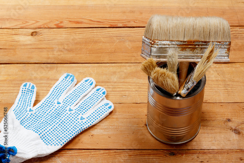 A metal jar with paint brushes and a glove on a wooden background of boards.