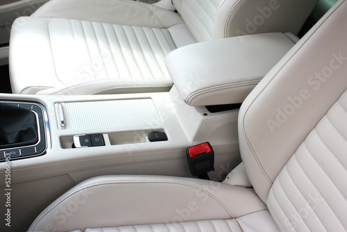 White leather interior of the luxury modern car. Leather comfortable white seats and armrest. Modern car interior details. Driver and passenger seats.