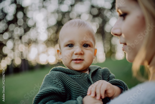 Mother holding her little baby son wearing knitted sweater during walk in nature.