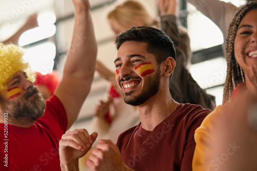 Excited football fans supproting spanish national team in live soccer match at stadium.