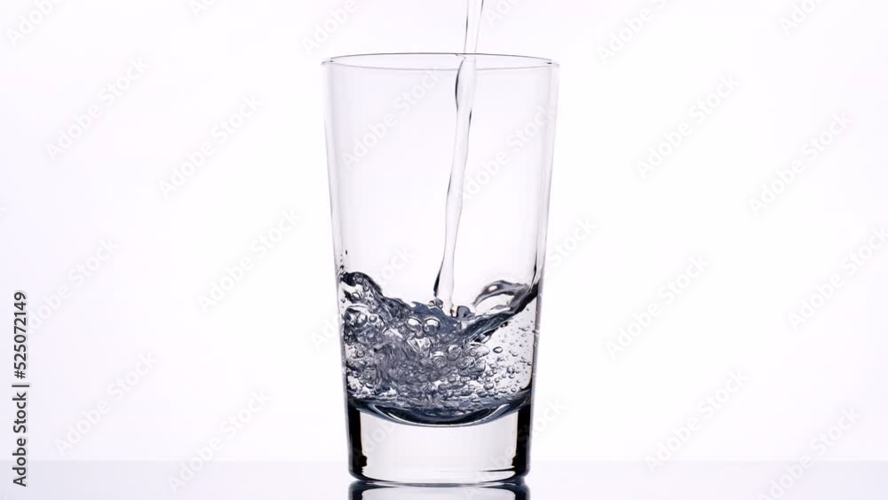 Pouring drink water to to glass of water. Close up pouring fresh clean drinking water into glass, splashing in glass on white background, soft focus with slow motion. Concept of drinking, healthy