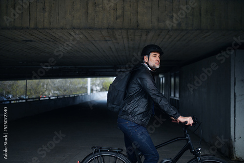 Businessman commuter on the way to work, riding bike under overpass, sustainable lifestyle concept. Dark background.
