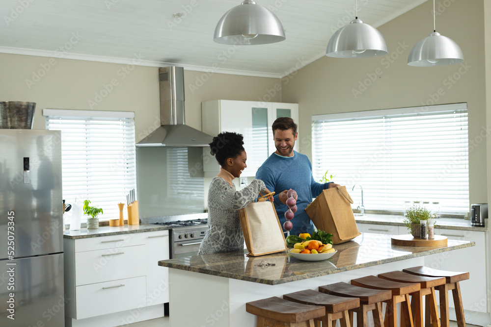 Image of happy diverse couple unpacking groceries in kitchen Image of happy diverse couple unpacking groceries in kitchen