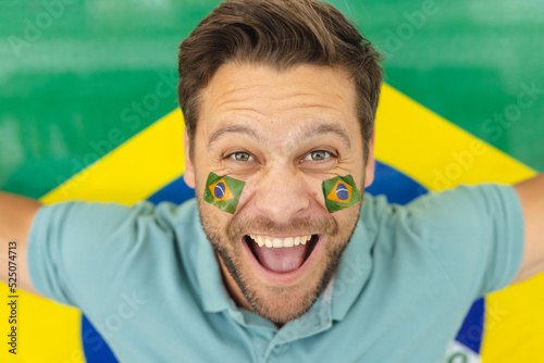 Image of happy caucasian man with flags of brazil on face over flag of brazil