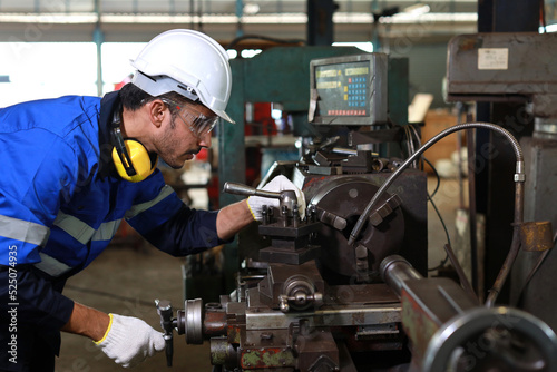 Technician engineer or worker man in protective uniform with safety hardhat maintenance operation or checking lathe metal machine at heavy industry manufacturing factory. Metalworking concept