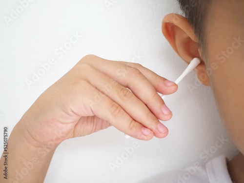 A boy cleans ear with a cotton swab. Closeup photo, blurred.