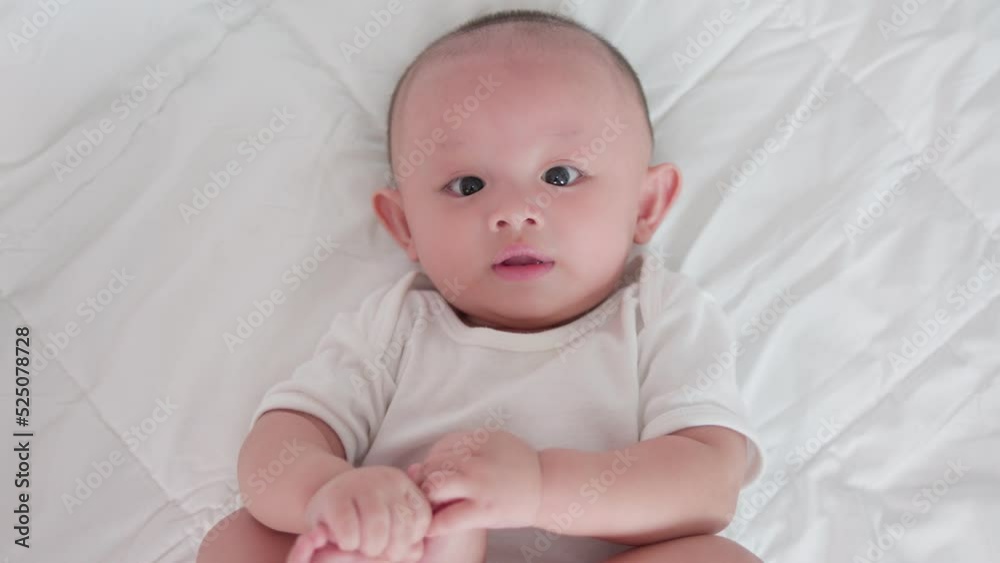 Portrait of cute asian newborn baby lying play on white bed look at camera with laughing smile happy face. Innocent little new infant adorable. Parenthood and Mother Day concept. Portrait of cute asian newborn baby lying play on white bed look at camera with laughing smile happy face. Innocent little new infant adorable. Parenthood and Mother Day concept.